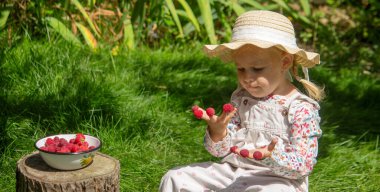 Bahçedeki küçük bir kız ahududu yiyor.