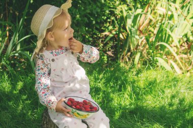 Bahçedeki küçük bir kız ahududu yiyor.