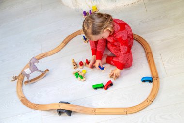 Child in Pajamas Playing with a Wooden Train Set under the Christmas Tree.