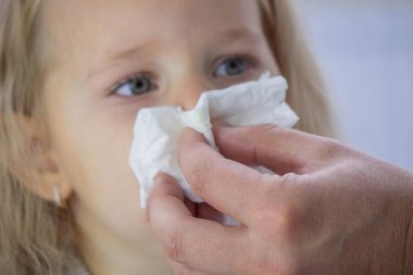 Parent's Hand Wiping a Sick Toddler Girl's Runny Nose with a Paper Tissue.