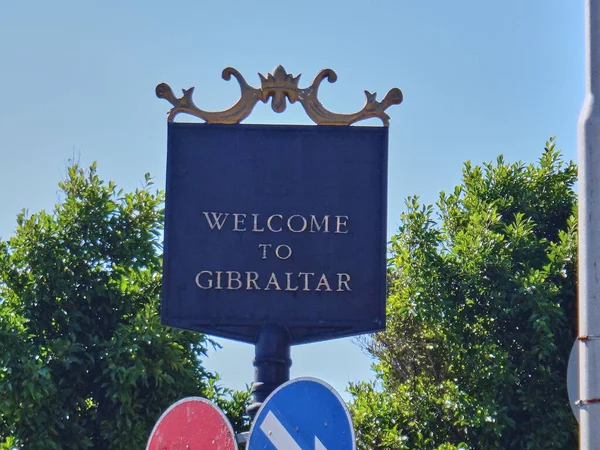 stock image Gibraltar, United Kingdom - 06 08 2014: black and golden metal sign in the british sovereign territory in Spain saying welcome to Gibraltar with the rock of Gibraltar in the background