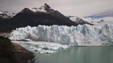 Perito Moreno Buzulu 'nun mavi buzu Patagonya, Arjantin' deki Glaciers Ulusal Parkı 'nda, Arjantin' in turkuvaz suyu ile ön planda koyu yeşil ormanlar ve And Dağları 'nın dağlarını örttü.