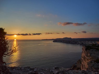 Bonifacio şehrinde gün batımı, Fransa 'nın Korsika adasındaki Akdeniz' in turkuaz suyuyla çevrili beyaz kayalıklarda uzanıyor.