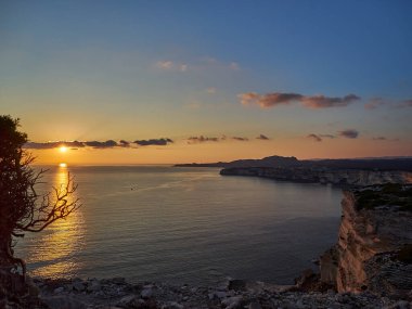 Bonifacio şehrinde gün batımı, Fransa 'nın Korsika adasındaki Akdeniz' in turkuaz suyuyla çevrili beyaz kayalıklarda uzanıyor.