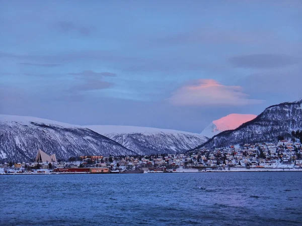 sunset over the cathedral in the winter landscape of the port of Tromso in a fjord at the coastline of northern Norway with snow covered mountains