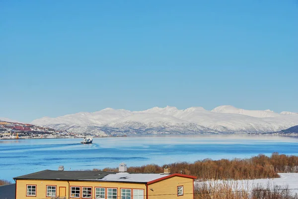 fishing boat in the winter landscape of the port of Tromso in a fjord at the coastline of northern Norway with snow covered mountains in the background