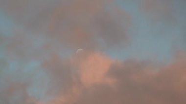 clouds lit up by the sunset moving in front of the moon in the clear blue sky at evening