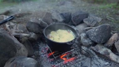 cast iron pot cooking a meal over an open camp fire next to a lake in the los alerces national park, Patagonia, Argentina.