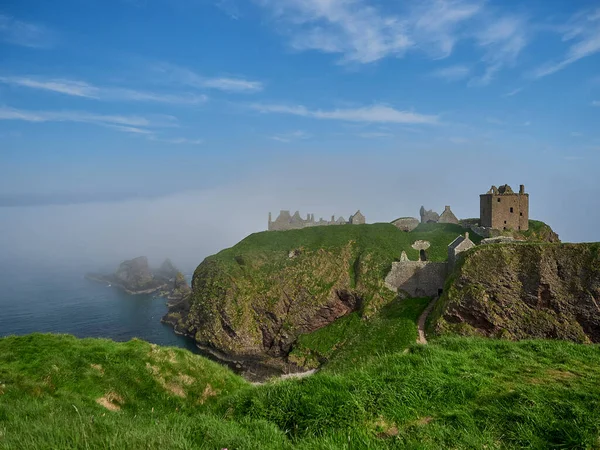 stock image Dunnattor Castle, Scotland - 05 21 2018: Dunnottar Castle sitting high on a steep cliff of the atlantic ocean coastline of Scotland on a sunny day with yellow gorse.