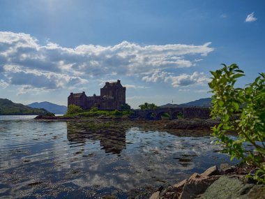 Eilean Donan, İskoçya - 05: 26 2018: Kuzey İskoçya kıyılarındaki tarihi ve tarihi bir Eilean şatosu. Güneşli bir günde Atlantik okyanusunun sakin sularında yansımaları var..