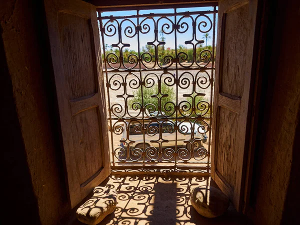 Kasbah 'ta bir terasın içindeki dövmeli demir bir pencereden bakıldığında, Kuzey Afrika' nın Fas çölünde, güzel bir vahada inşa edilmiş, tipik ve geleneksel bir kil ve samandan yapılmış bir bina görülüyor..