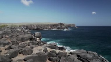 Derin mavi Pasifik Okyanusu 'nun dalgaları güneşli bir günde Galapagos adalarının siyah volkanik lav kayaları üzerinde kıyıya vuruyor..