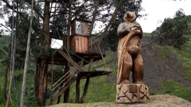 Gözlüklü bir ayının ahşap heykeli, Tremarctos ornatus, Andean dağlarındaki dağların ormanlarına özgü, Ekvador 'daki Oso Andino rezervindeki ormandaki yüksek bir ağaçtan tırmanarak.