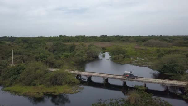 ブラジル 不法森林火災による森林破壊によって脅かされる熱帯湿地パンタナールのトランスパンタニラで木製の橋を渡る4X4オフロードカーの空中ドローンビュー — ストック動画