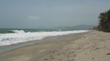Dalgalar, Kolombiya 'daki Sierra Nevada de Santa Marta' daki Atlantik Okyanusu 'nun tropikal kıyısı boyunca Tayrona Ulusal Parkı yakınlarındaki beyaz kumsala çarpıyor..