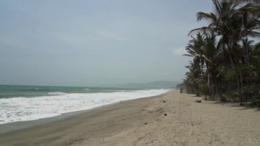 Dalgalar, Kolombiya 'daki Sierra Nevada de Santa Marta' daki Atlantik Okyanusu 'nun tropikal kıyısı boyunca Tayrona Ulusal Parkı yakınlarındaki beyaz kumsala çarpıyor..