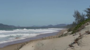 Okyanus kıyısındaki Florianolpolis yakınlarındaki Ilha Santa Catarina tropikal manzarası boyunca uzanan güzel ve cennet gibi beyaz kumsalda dalgalar kıyıya vuruyor..