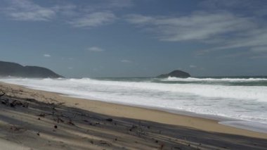 Okyanus kıyısındaki Florianolpolis yakınlarındaki Ilha Santa Catarina tropikal manzarası boyunca uzanan güzel ve cennet gibi beyaz kumsalda dalgalar kıyıya vuruyor..