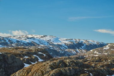 Norveç 'te güneşli bir günde Lysebotn yolu boyunca buzla kaplı buzlu ve arka planda karla kaplı cennet gibi bir dağ gölü..