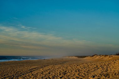 Dalgalar, Portekiz 'in Porto yakınlarındaki Atlantik Okyanusu' nun sahil şeridi boyunca uzanan plajda romantik bir gün batımında kıyıya vuruyor..