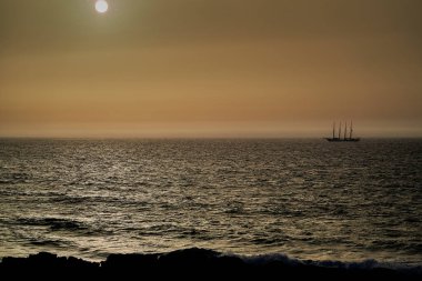 Dört direkli yelkenli gemi, romantik günbatımında derin mavi Atlantik okyanusunu geçerek Porto yakınlarındaki bir sahil şeridinde dramatik bir gökyüzünün olduğu altın saat boyunca.