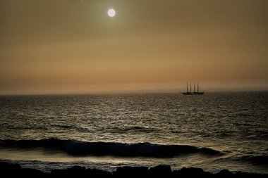 Dört direkli yelkenli gemi, romantik günbatımında derin mavi Atlantik okyanusunu geçerek Porto yakınlarındaki bir sahil şeridinde dramatik bir gökyüzünün olduğu altın saat boyunca.