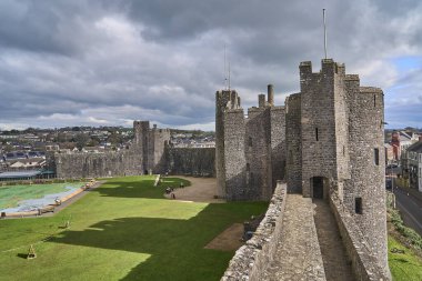 Pembroke, Wales - 02 28 2023: Altında su olan binalarla çevrili yeşil bir tepedeki eski ortaçağ Pembroke kalesi