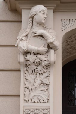 Güzel bir Art Nouveau heykeli genç bir kadın heykeli. Ayrıntılı figür, omuzlarının üzerinden dökülen uzun saçlı, süslü bir korbel üzerinde duruyor. Corbel, Ar 'ın tipik çiçek motifleri ve büyük ayçiçeği yapraklarıyla süslenmiştir.