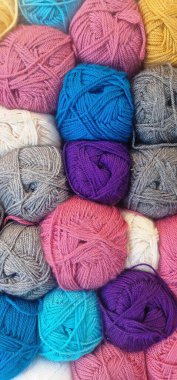 çeşitli renkli iplik topları. Renkler arasında pembe, gri, beyaz, mavi, turkuaz, mor ve sarı yer alıyor. İplik toplarından bazıları renk karışımı gibi görünüyor. Doku yumuşak ve tüylü, bazı gevşek iplikler görülebilir..