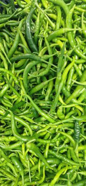 Büyük bir yeşil biber yığınının tam kare görüntüsü, biberler uzun ve bazıları kıvrımlı, bazıları koyu yeşil, gölgeler ve dokular karışımı oluşturuyor.