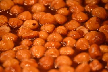 Yüksek açılı, yakın plan bir çekim sıcak, turuncu-kahverengi bir yahniye odaklanır. Düzinelerce parlak, yuvarlak yiyecek çerçeveyi dolduruyor, muhtemelen kestaneler, kalın ve parlak bir sosa batırılmış..