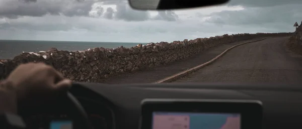 Driving along a rocky road along the coast of the ocean. Driving a car on the road, from inside the car.