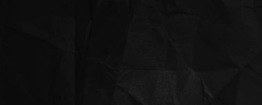Black background of crumpled paper in the dark. Wide panoramic black background with space for design. Web banner, website header.