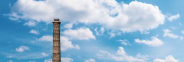 A large brick chimney against a blue cloudy sky. Industry and ecology concept banner with free space for text, copy space.