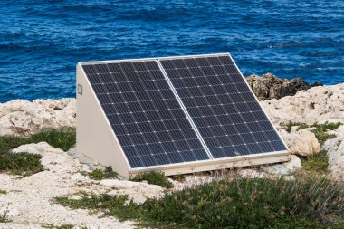 Deniz kıyısındaki kayalıklarda güneş panelleri. Doğa dostu enerji üretimi, doğa korumanın bir sembolü..