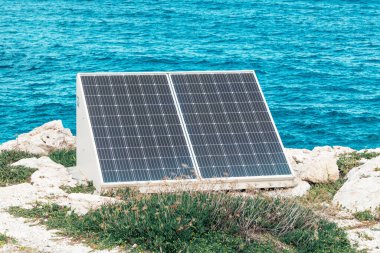 Güneş panelleri güneşe 45 derecelik bir açıyla yerleştirilmiştir. Güneşli bir hava, arka planda mavi su olan bir deniz.