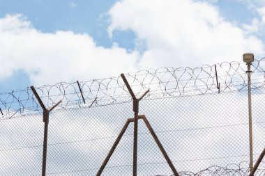 Dikenli tellerin yakın çekimi. Yüksek metal çitler ve dikenli tellerle çevrili korunan bir bölge..