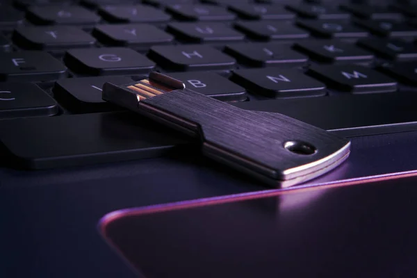 USB bellek çubuğu dizüstü bilgisayarın klavyesinde yakın plan bir anahtar şeklinde. Menekşe, mor ışık, yumuşak odak.