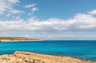 Kayalık körfez arasındaki mavi lagünün doğa manzarası. Güneşli bir günde turkuaz mavi suyla deniz manzarası, arkasında beyaz bulutlar olan mavi gökyüzü..