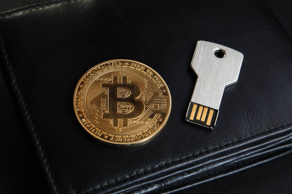 Bitcoin coin and USB flash drive in the form of a metal key on a black leather wallet. Cryptocurrency storage concept, cryptocurrency wallet.
