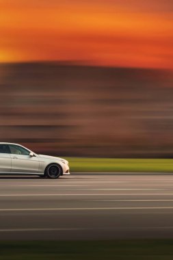 Hızlı bir araba. Geceleyin turuncu gökyüzü ile soyut hız bulanıklığı olan bir araba. Arabanın önü yan görünüyor..