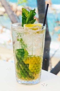 Limon ve yeşil nane yapraklı mojito kokteyli. Arka planda bulanıklık olan bardakta iç.