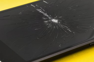 Sarı arka planda kırık ekranlı cep telefonu..
