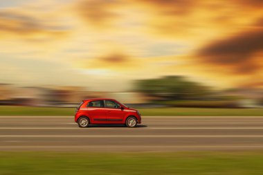 Küçük kırmızı araba. Günbatımı renklerinde asfalt sokakta hızlı giden araba ve metin için boş alan ile hareket bulanık arkaplan, kopyala.