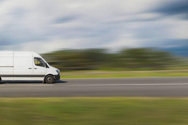 Грузовой фургон на размытом фоне. Белый грузовой фургон едет по улице с размытым фоном. Транспорт, логистическая концепция с свободным пространством для текста, копировальное пространство.