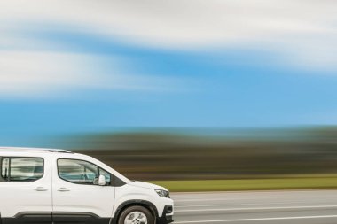 Beyaz minibüs caddede ilerliyor, hız arkaplanı bulanık.