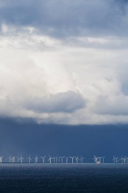 Offshore rüzgar çiftliği. Okyanustaki rüzgar türbini parkının dramatik manzarası. Arka planda büyük bulutlar var..