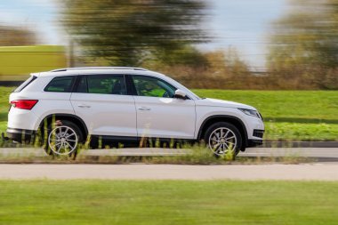 Beyaz SUV yolda ilerliyor. Güneşli havada hareket eden bir arabanın yan görüntüsü.