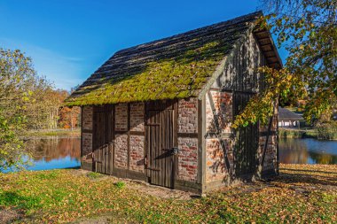 Sonbaharda göletin yanında yosun kaplı çatısı olan eski tuğla kulübe..