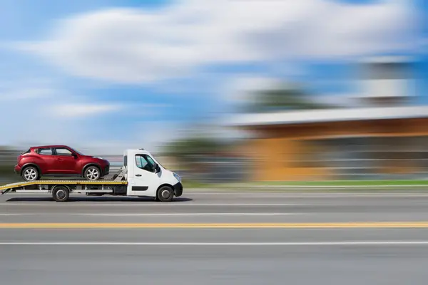 Bir çekici bir araba naklediyor. Bulanık bir arkaplanda platformda araba taşıyan hareket halindeki bir çekicinin yan görüntüsü.